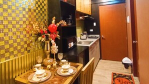 A compact kitchen with a tiled backsplash, a dining table set with plates and glasses, and a small refrigerator. - Cappuccino Studio in Mesavirre Garden Bacolod (Bacolod)
