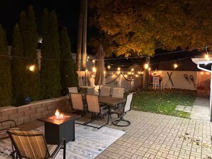 An outdoor patio area with a fire feature, seating, and string lights.