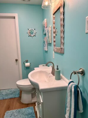 A bathroom with a toilet, sink, and mirror. There are towels hanging on the wall and a rug on the floor.