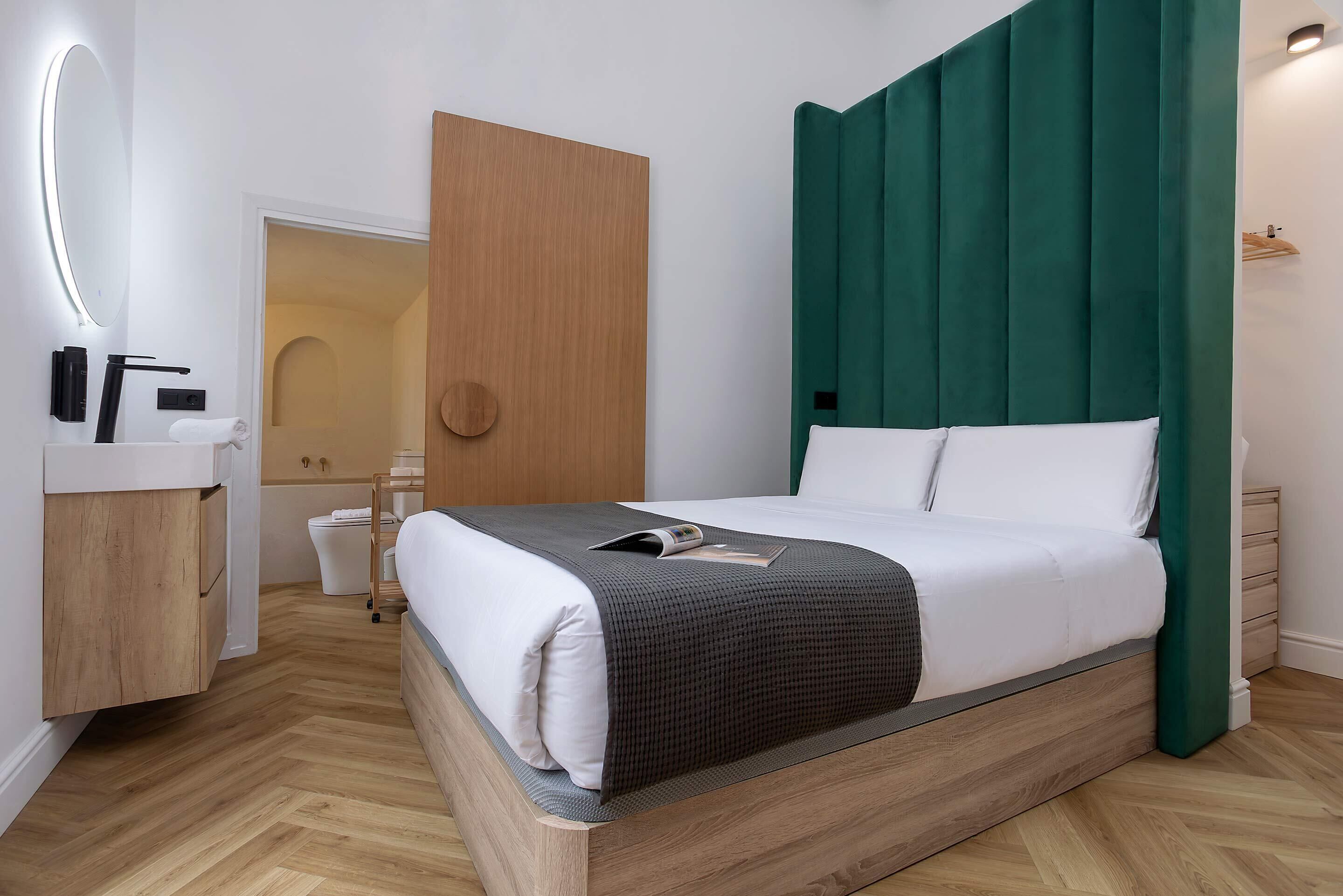 A modern bedroom with a wooden bed frame, a large mirror, a bedside table, and a green headboard.