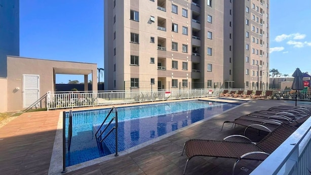 En swimmingpool med solstolar, en modern byggnad och en klar himmel.