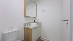 Un bany petit amb un vàter, un lavabo i un mirall damunt, i un armari de fusta a sota.