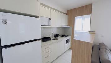 Cozinha compacta com geladeira, micro-ondas, pia, fogão e detalhes em madeira.