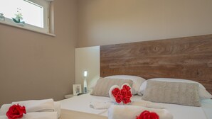 Una habitación de hotel con una cama bien hecha, sábanas blancas y rosas rojas como elementos decorativos.