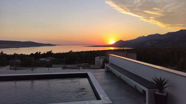 Piscina en la azotea con vistas a una puesta de sol sobre un cuerpo de agua y montañas.