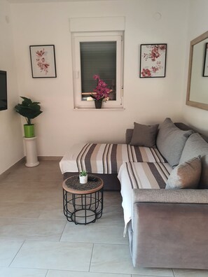 Una sala moderna con un sofá, una mesita redonda con una planta, otra planta en maceta y dos cuadros con motivos florales en la pared.