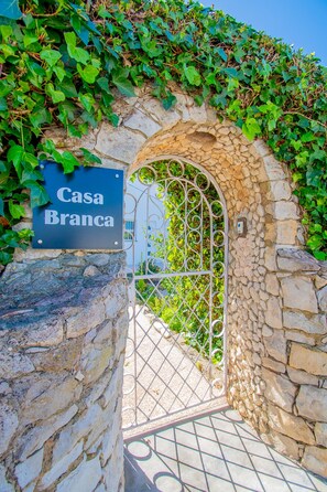 A stone archway with a metal gate, a sign reading "Casa Blanca," and lush green foliage. - Casa Branca in Carvoeiro (Lagoa)