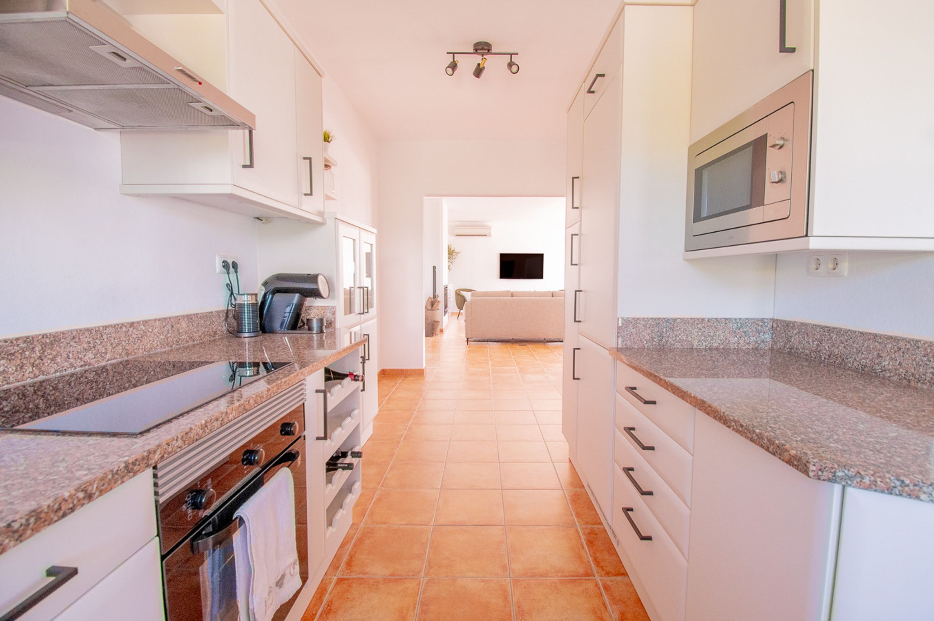 A narrow kitchen with white cabinets, a built-in oven, and a microwave.