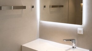 Uma casa de banho moderna com uma pia branca, um espelho com iluminação integrada e um porta-toalhas fixado na parede.