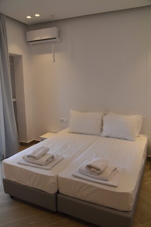 A double bed with two pillows and folded towels, a bedside table, and an air conditioning unit mounted on the wall. - Ela Mare Hotel (Malia)
