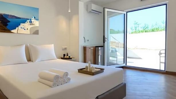 Quarto de hotel com uma cama, um quadro, uma pequena mesa com flores e vista através de uma porta de vidro.