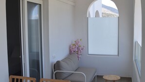 Quarto pequeno com uma mesa de jantar, duas cadeiras de madeira, um sofá, um banquinho e uma janela com vista em arco.