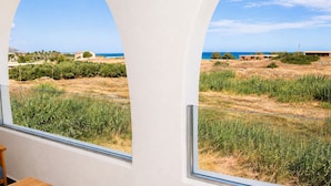 Quarto com uma grande janela arqueada com vista para a paisagem costeira, vegetação e edifícios ao longe.