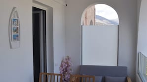 Quarto pequeno e moderno com uma mesa de jantar e cadeiras de madeira, um sofá cinza e vista para o exterior por uma janela em arco.