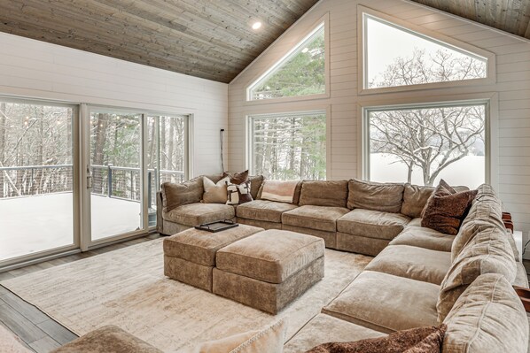 A spacious living room with a large sectional sofa, a small ottoman, and a sliding glass door leading to an outdoor deck.
