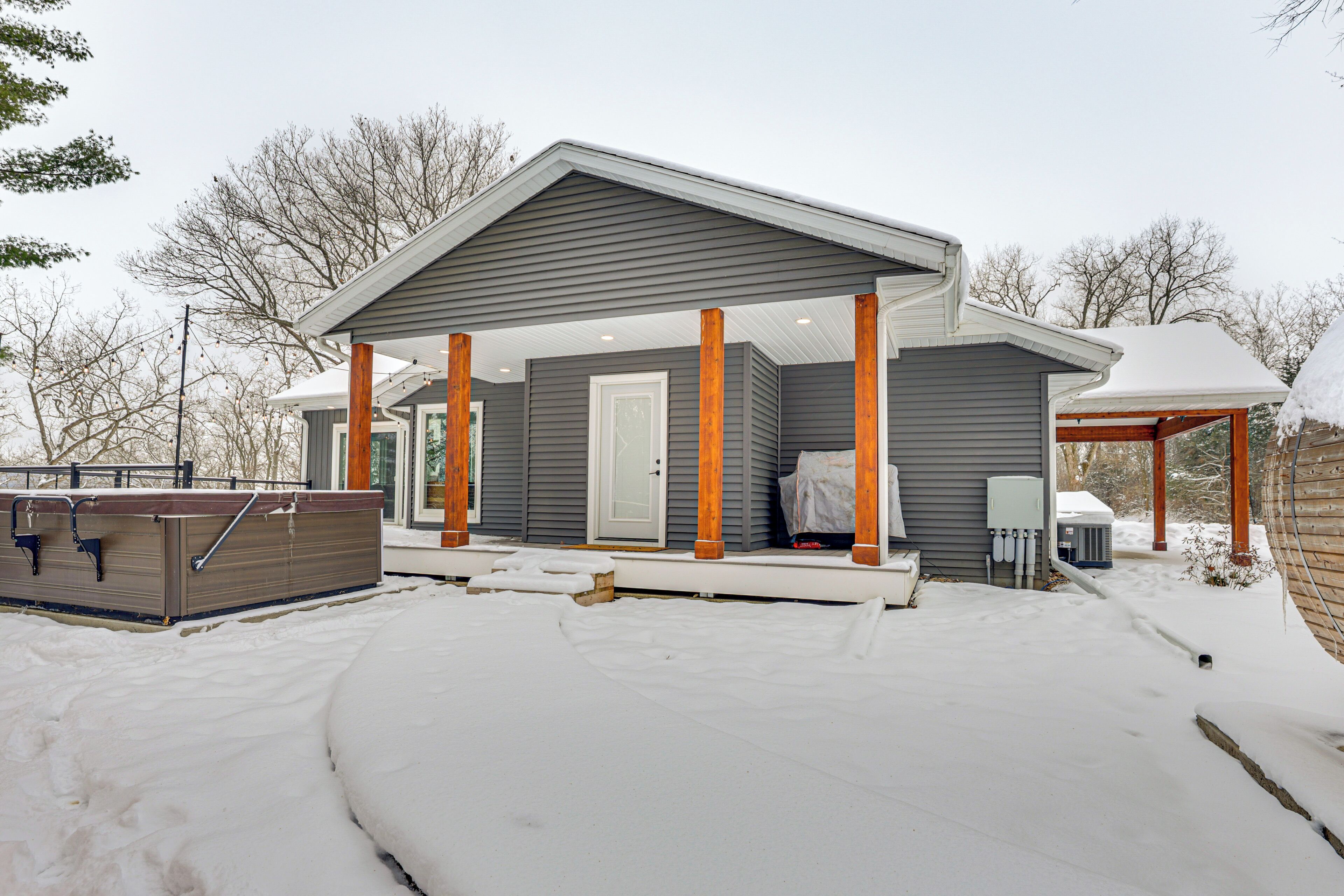 A modern house with a covered porch, a hot tub, and a snow-covered yard.