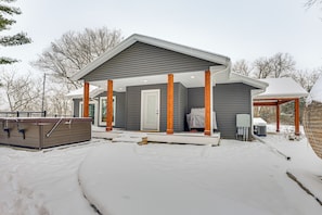 A modern house with a covered porch, a hot tub, and a snow-covered yard.