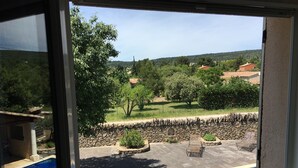 A view through a window of a swimming pool, stone wall, and greenery. - Country House 'Mas Les Coutilles' with Mountain View, Private Pool and Wi-Fi (Cabrières-d'Avignon)