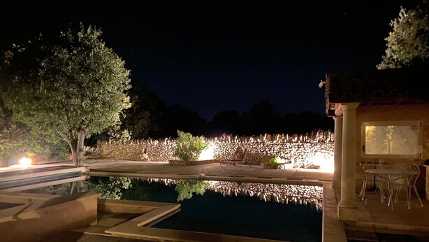 A nighttime outdoor swimming pool area with a stone wall, a tree, and a small building with a window. - Country House 'Mas Les Coutilles' with Mountain View, Private Pool and Wi-Fi (Cabrières-d'Avignon)