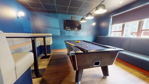 A pool table in a room with blue walls, a television mounted above it, and seating areas. - iQ Student Quarter in Salford (Salford)