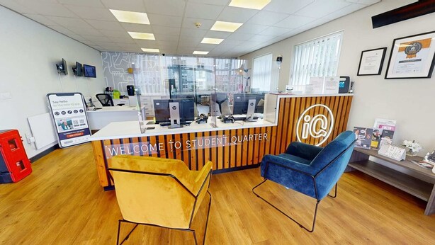 A reception area with a wooden desk, two chairs, and a glass partition. - iQ Student Quarter in Salford (Salford)