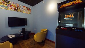 A room with a large screen TV, a GamePro arcade machine, a small table, and a yellow chair. - iQ Student Quarter in Salford (Salford)