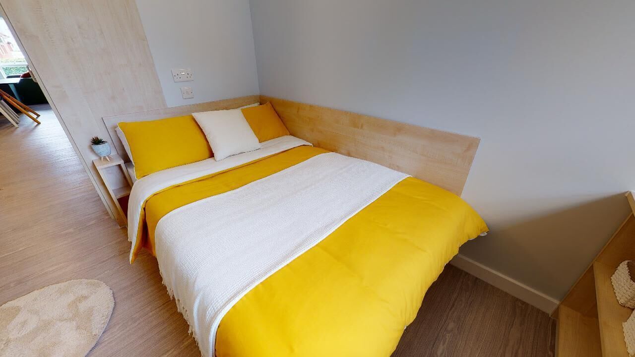 A bed with a wooden headboard, a white and yellow bedspread, and a small bedside table with a lamp.
