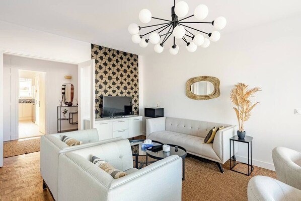 Ein modernes Wohnzimmer mit einem Ecksofa, einem Couchtisch, einem Fernseher und einer außergewöhnlichen Deckenleuchte.