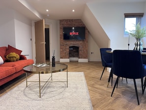 A modern living room with a red sofa, a glass coffee table, a brick fireplace, and a TV mounted on the wall.
