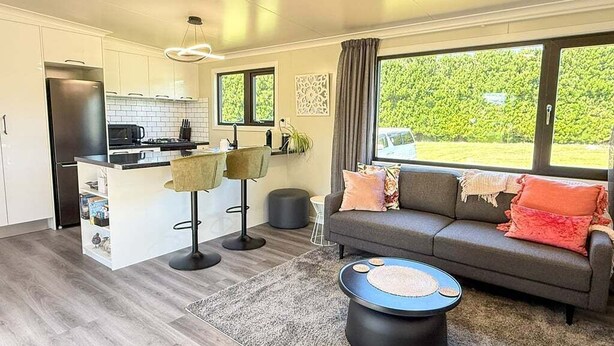 A modern kitchen with white cabinets, a central island, and a dining area with a grey sofa and coffee table. - Private 2BR Haven – West Melton - Haven on Halkett (Christchurch)