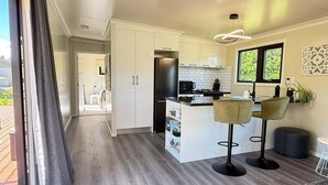 A modern kitchen with white cabinets, a stainless steel refrigerator, and a bar area with two stools. - Private 2BR Haven – West Melton - Haven on Halkett (Christchurch)