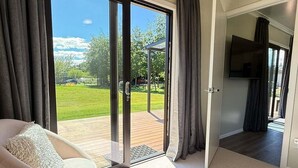 A room with a sliding glass door leading to an outdoor deck, a sofa with a fluffy pillow, and a television mounted on the wall. - Private 2BR Haven – West Melton - Haven on Halkett (Christchurch)