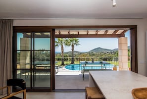 A modern room with a large sliding glass door leading to an outdoor pool area with a view of hills.