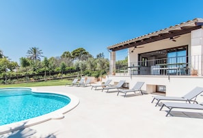 A swimming pool with lounge chairs, a building with large windows, and a clear blue sky.