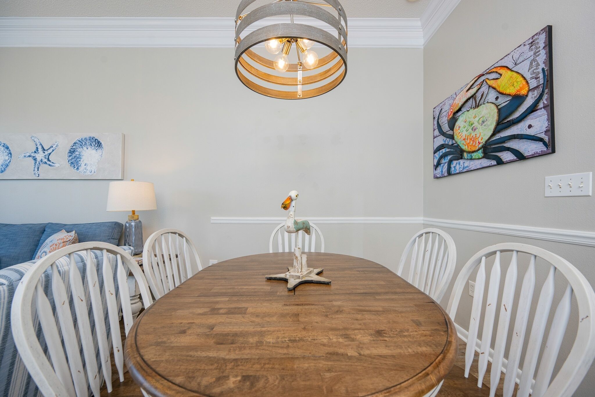 A dining area with a wooden table, white chairs, a hanging light fixture, and wall art.