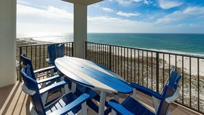 A balcony with a table and chairs, overlooking a beach and ocean. - Phoenix Vi 61406 2 Bedroom Condo (Orange Beach)