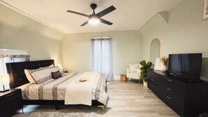 A bedroom with a bed, a TV, a dresser, a ceiling fan, and a window with curtains. - Newly remodeled 3 bedroom, 1.5 bath home with a river view in downtown Elkhart.  (Elkhart)