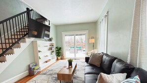 A living room with a black leather sofa, a wooden coffee table, a bookshelf, and a staircase. - Newly remodeled 3 bedroom, 1.5 bath home with a river view in downtown Elkhart.  (Elkhart)