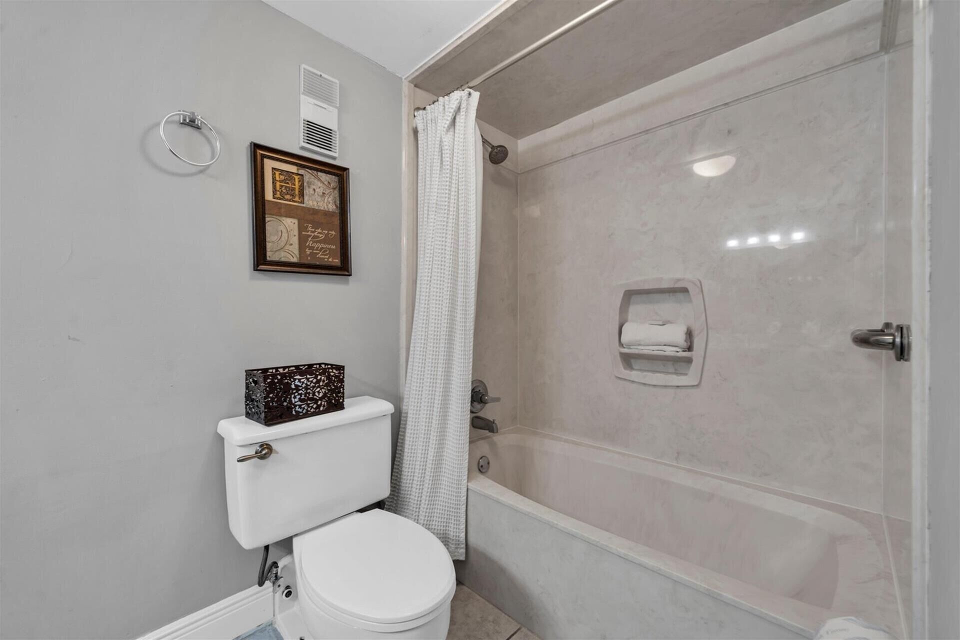 Ein Badezimmer mit Toilette, einer Dusche mit Glastür, einem Handtuchspender und einem gerahmten Bild an der Wand.