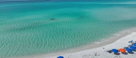 Una playa con agua turquesa cristalina, una orilla arenosa y varias sombrillas azules.