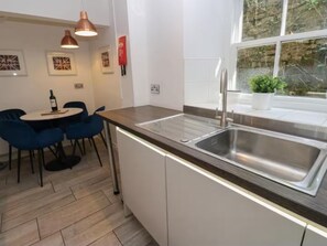Eine moderne Küche mit einer Edelstahlspüle, einem runden Tisch mit Stühlen, Pendelleuchten und gerahmten Kunstwerken an der Wand.