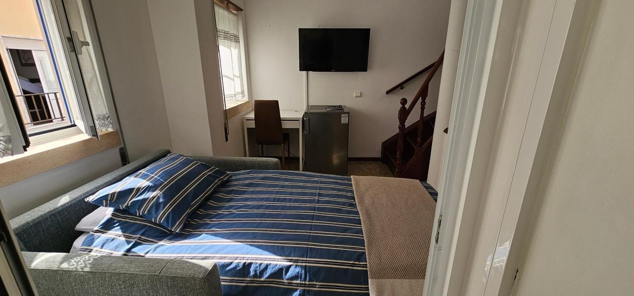 A bedroom with a bed, a desk, a chair, a television, and a window.