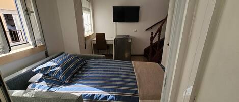 A bedroom with a bed, a desk, a chair, a television, and a window.