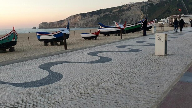 Une plage où des bateaux sont exposés et où l’on trouve une promenade dallée aux motifs décoratifs.