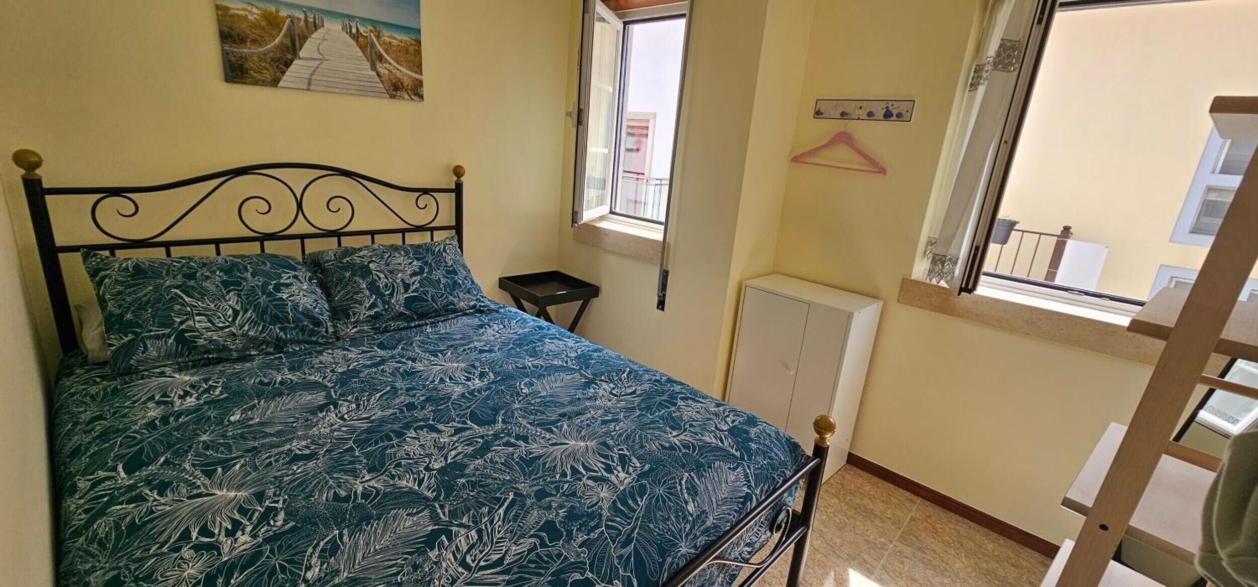 Une chambre à coucher avec un lit, une fenêtre, un radiateur et un porte-manteau fixé au mur.
