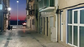 Une rue pavée bordée de bâtiments des deux côtés, un lampadaire et un coucher de soleil à l’horizon.