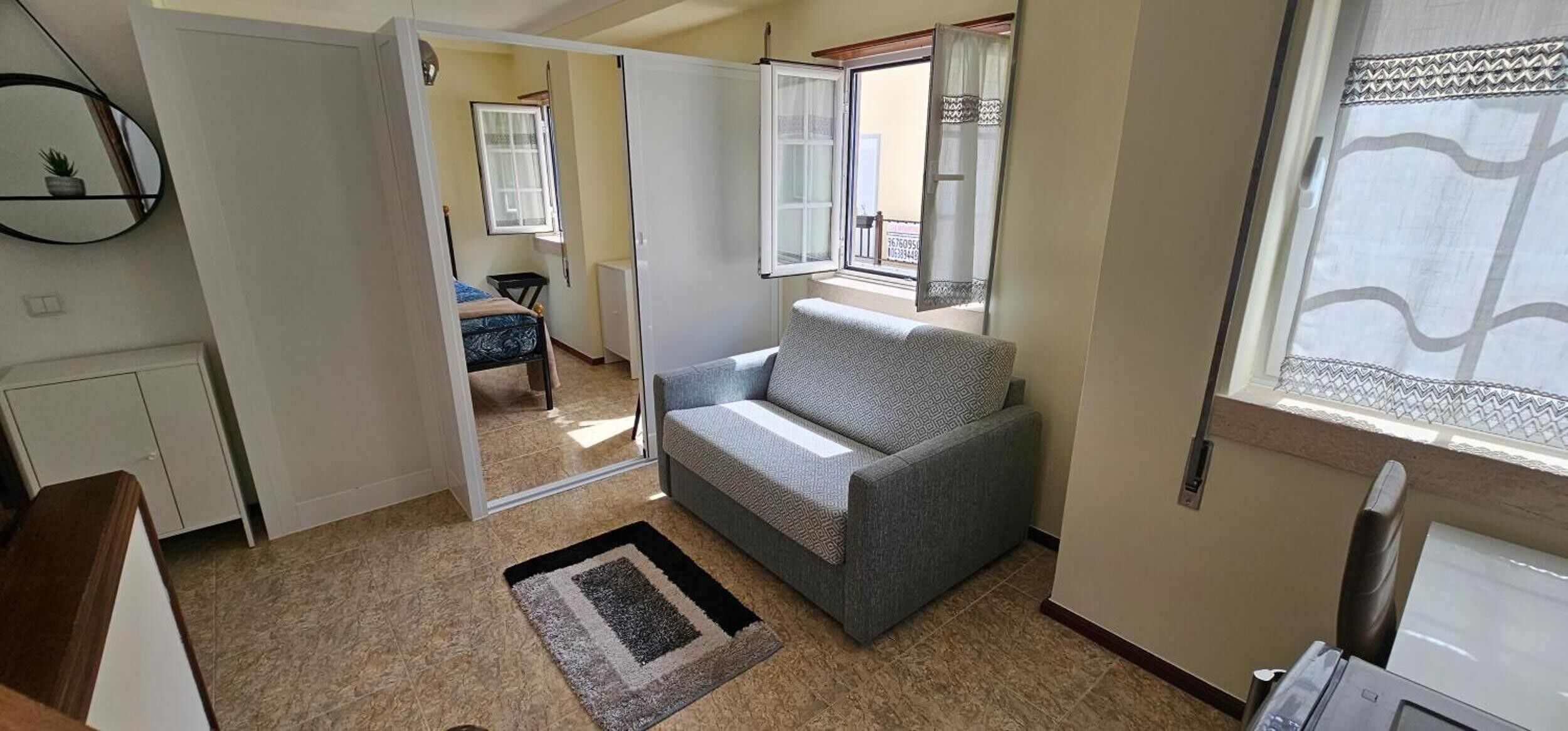 Un espacio habitable compacto con sofá, una mesita, una silla y una ventana con cortinas.