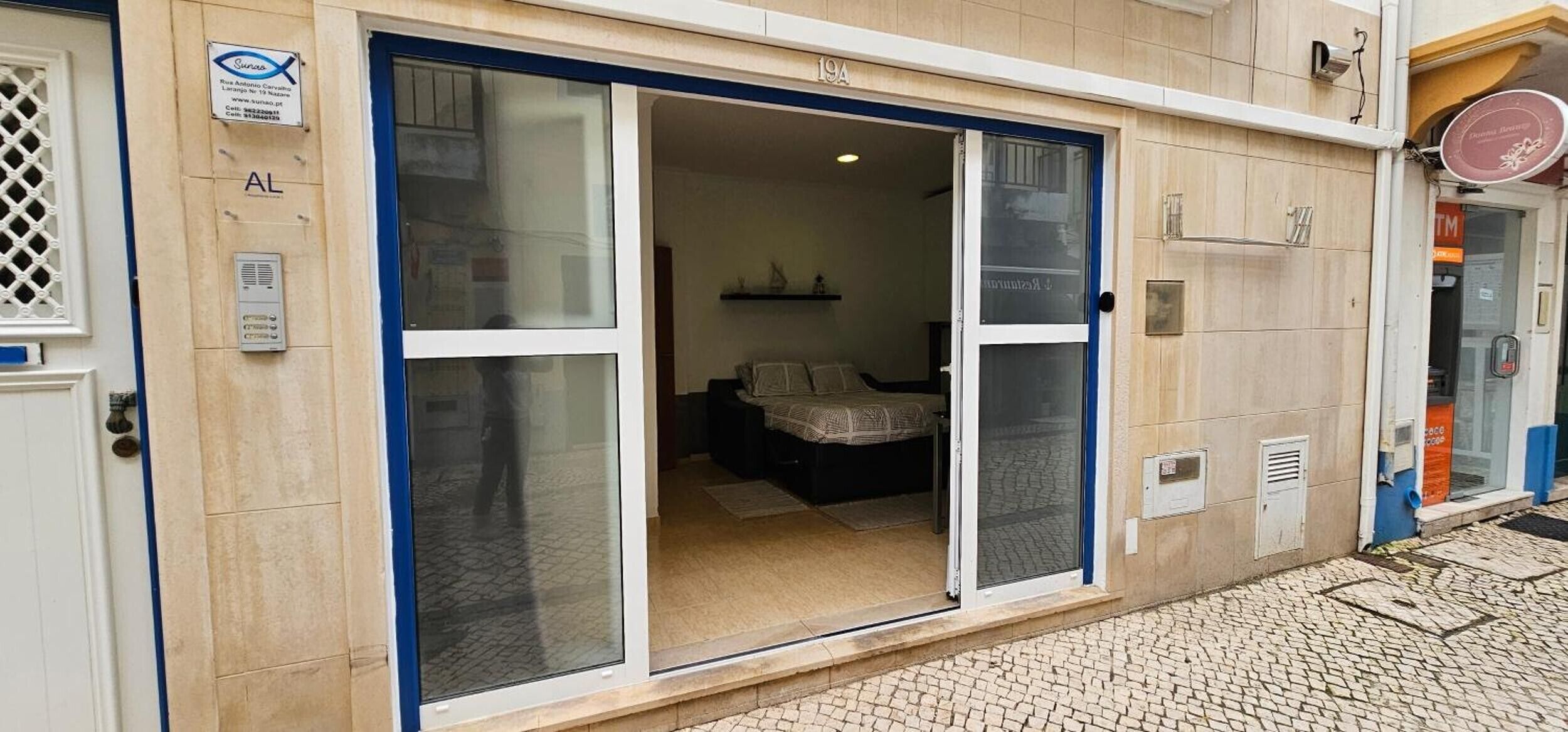 A hotel entrance with a sliding glass door, a bed visible inside, and a sign with the number '19A' above the door.