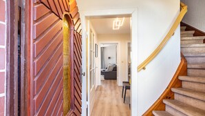 Escada que leva a uma sala de estar, com corrimão de madeira e piso coberto por carpete.