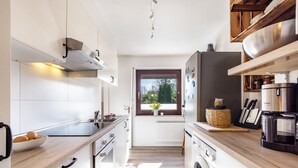 Uma cozinha moderna com armários brancos, forno embutido, máquina de lavar e janela com vista para vegetação.